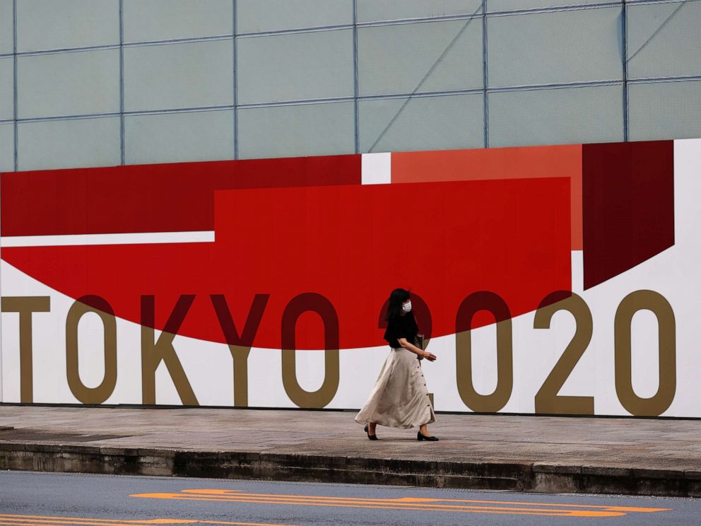 PHOTO: A woman, wearing a protective mask against COVID-19, walks past a wall bearing logo of Tokyo 2020 Olympic Games in Tokyo, Japan, July 29, 2021.   REUTERS/Kim Kyung-Hoon