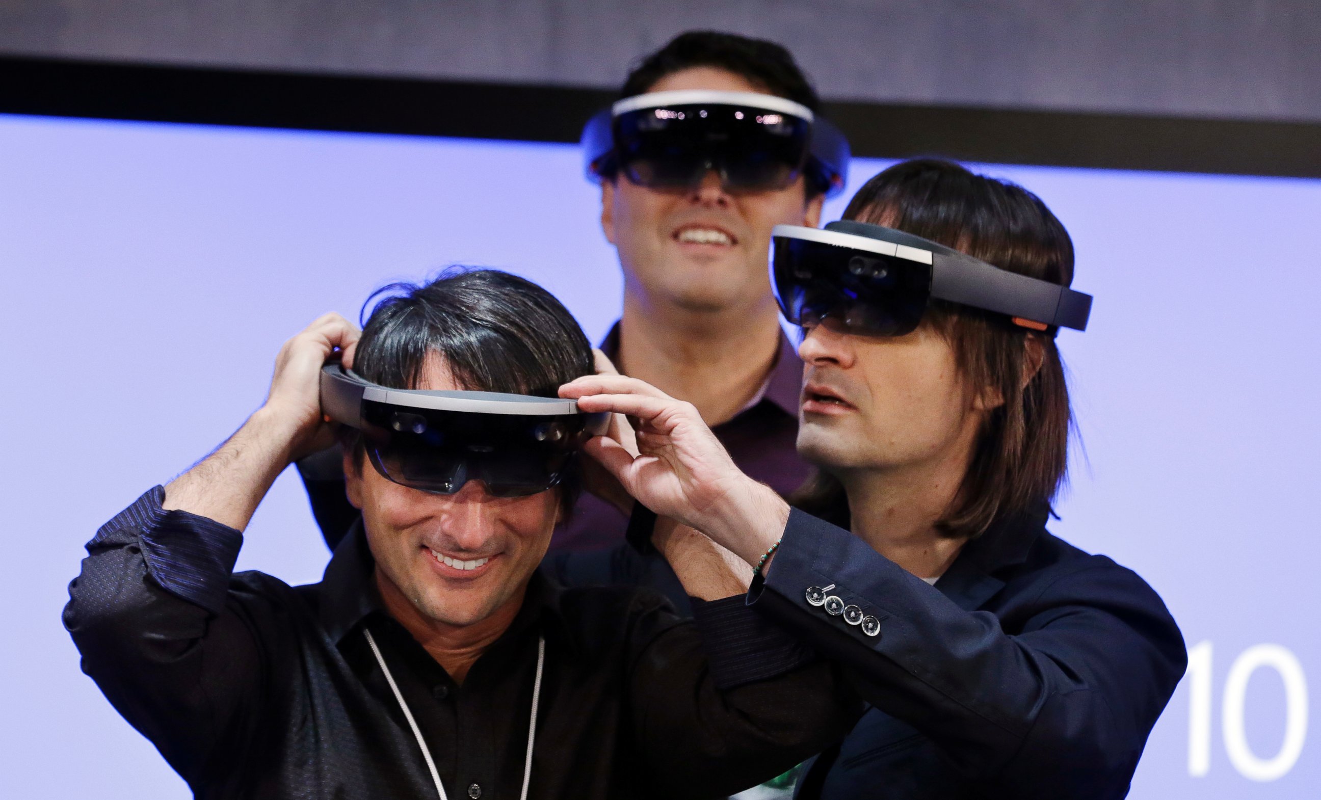 PHOTO: Microsoft's Joe Belfiore (L) smiles as he tries on a "Hololens" device with colleagues Alex Kipman (R) and Terry Myerson following an event demonstrating new features of Windows 10 at the company's headquarters on Jan. 21, 2015, in Redmond, Wash.