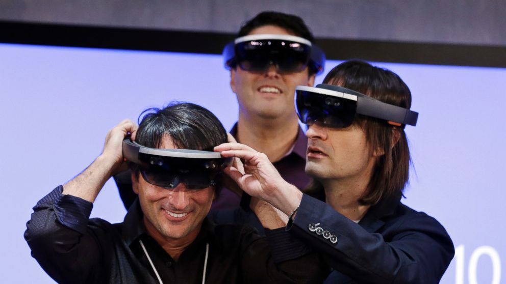 Microsoft's Joe Belfiore, left, smiles as he tries on a "Hololens" device with colleagues Alex Kipman, right, and Terry Myerson following an event demonstrating new features of Windows 10 at the company's headquarters on Jan. 21, 2015, in Redmond, Wash.