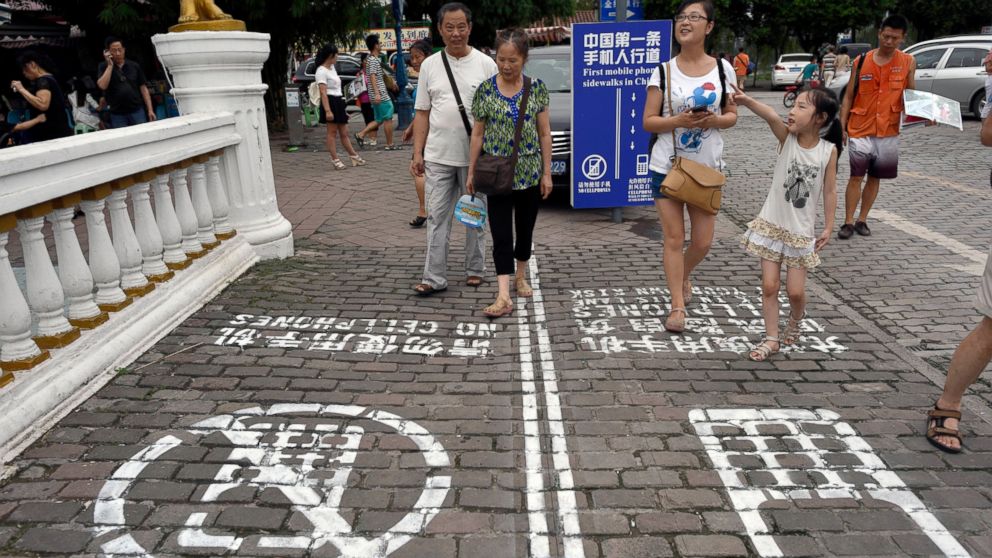 Residents look at a sign with the words "China's First Cellphone Lane" explaining the use of a lane which separates those using their phones as they walk from others in China's Chongqing Municipality, Sept. 13, 2014. 