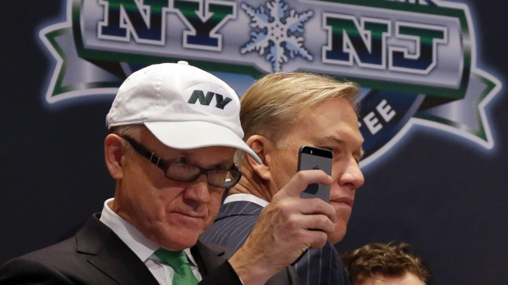 New York Jets owner Woody Johnson, left, uses his mobile phone to photograph from the podium before New York Stock Exchange opening bell ceremonies in New York, Jan. 30, 2014.