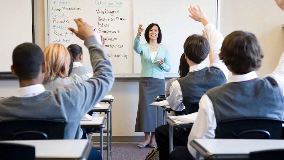 Students in class raise their hands to answer a question.