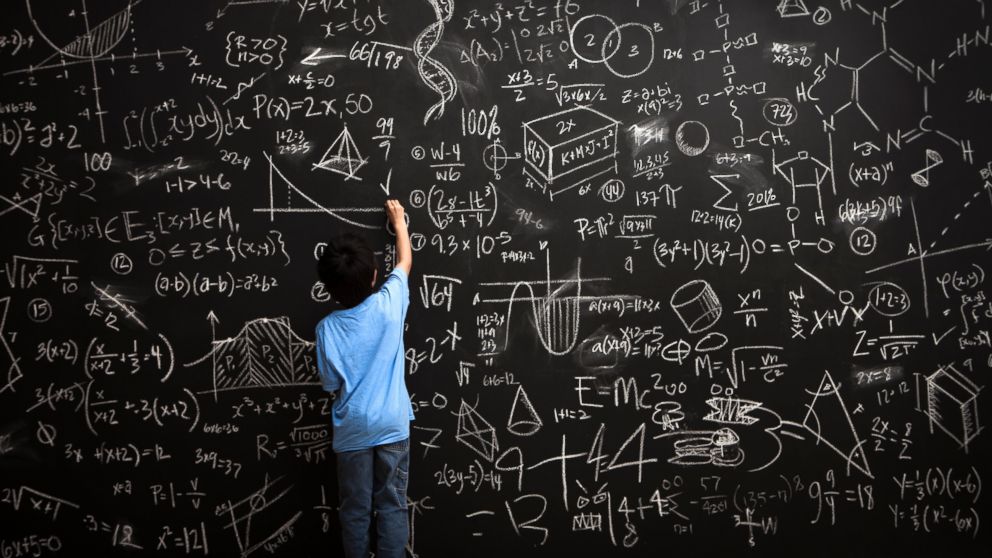 A young boy writes math equations on chalkboard.