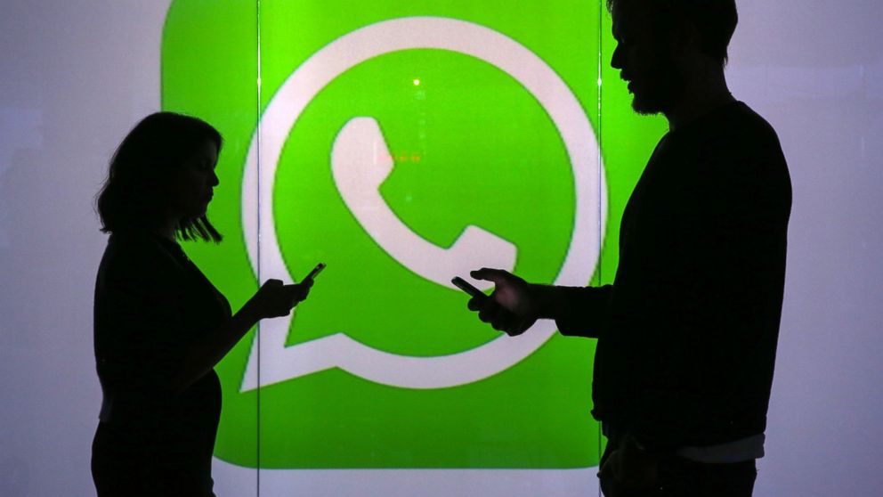 People are seen as silhouettes as they check mobile devices while standing against an illuminated wall bearing WhatsApp Inc's logo in this arranged photograph in London, Jan. 5, 2016.  
