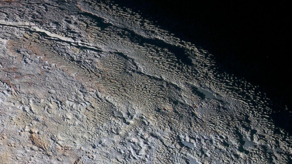In this extended color image of Pluto taken by NASA’s New Horizons spacecraft, rounded and bizarrely textured mountains rise up along Pluto and show intricate but puzzling patterns of blue-gray ridges and reddish material in between.