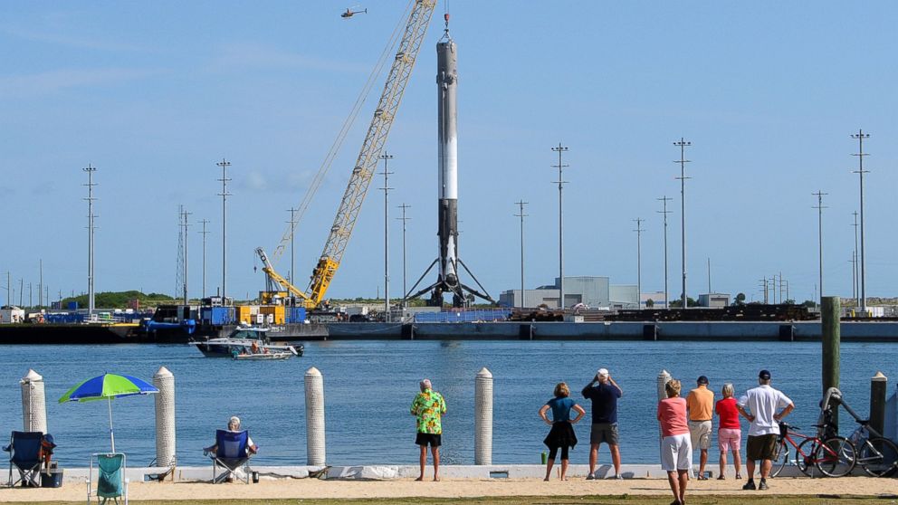People watch as the first stage of a SpaceX Falcon 9 rocket is hoisted by a crane at Port Canaveral, Florida after returning to port overnight on a drone barge. The rocket successfully landed on the barge for the first time on April 8, 2016 after being launched from Cape Canaveral.