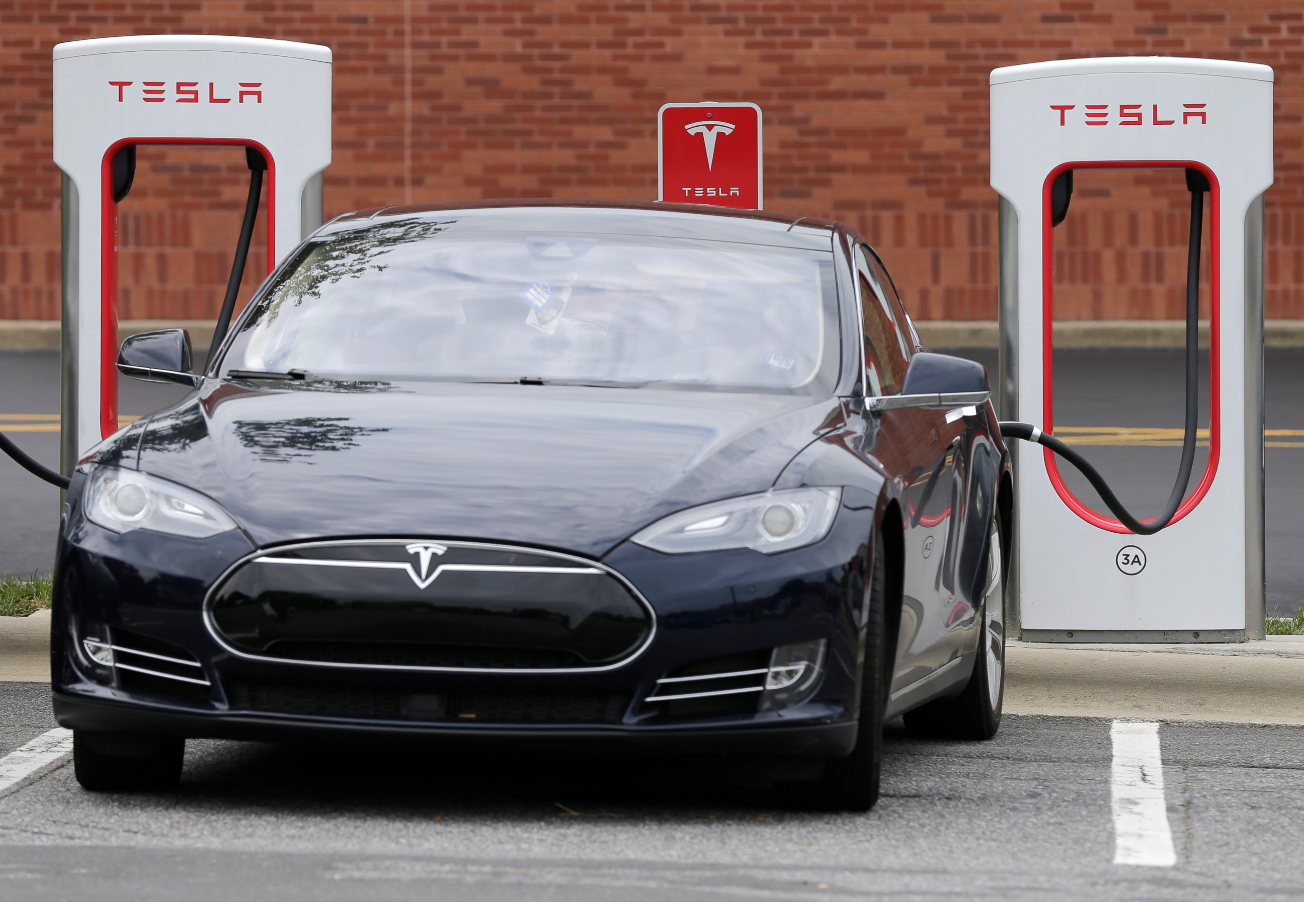 FILE- In this June 24, 2017, file photo, a Telsa Model 3 car recharges at a Tesla charging station at Cochran Commons shopping center in Charlotte, N.C. esla has cut $1,100 from the base price of its Model 3 car designed for the mass market. The elec