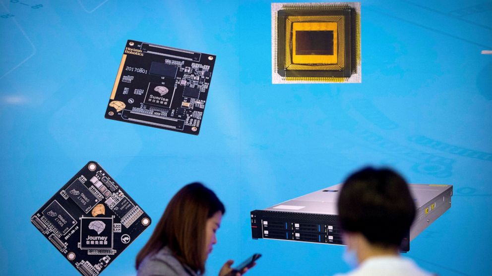 FILE - In this May 18, 2018, file photo, visitors walk past a display showing microchips and circuit boards at the 21st China Beijing International High-tech Expo in Beijing. For four decades, Beijing has cajoled or pressured foreign companies to han