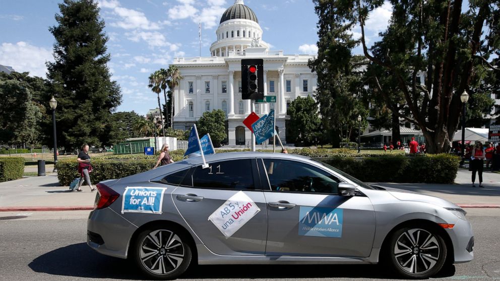 In this Aug. 28, 2019, photo, supporters of a measure to limit when companies can label workers as independent contractors drive their cars past the Capitol during a rally in Sacramento, Calif. California lawmakers are debating a bill that would make