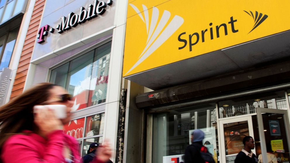 FILE - In this April 27, 2010 file photo, a woman using a cell phone walks past T-Mobile and Sprint stores in New York. T-Mobile, in its attempt to buy Sprint for $26.5 billion, shrinking the major wireless companies to three from four and creating a