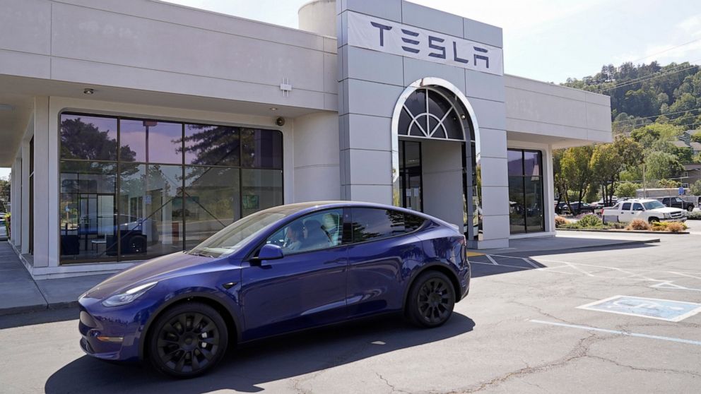 FILE - In this April 2, 2021 file photo two women in an electric car drive into a Tesla delivery location and service center in Corte Madera, Calif. California’s Department of Motor Vehicles is reviewing whether Tesla is violating a state regulation 