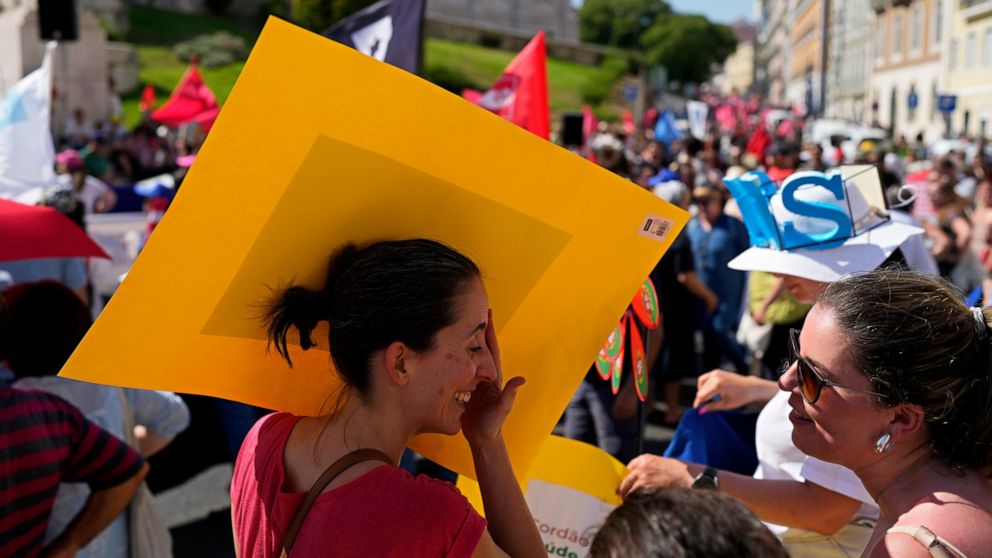 A protestor shades herself from the sun behind her poster in hot weather during a demonstration by workers' unions outside the parliament in Lisbon, Thursday, July 7, 2022. Portugal is bracing for a heat wave, with temperatures in some areas forecast