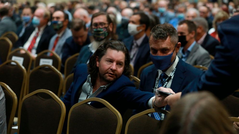 An attendee at the annual meeting of the New Mexico Oil And Gas Association reaches for a mask after the crowd was reminded to wear them by the state's governor, Monday, Oct. 4, 2021, in Santa Fe, New Mexico. Democratic Gov. Michelle Lujan Grisham ad