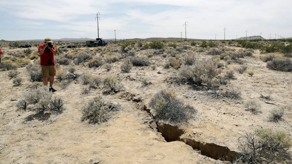 A visitor takes a photo of a crack on the ground following recent earthquakes Sunday, July 7, 2019, outside of Ridgecrest, Calif. (AP Photo/Marcio Jose Sanchez)