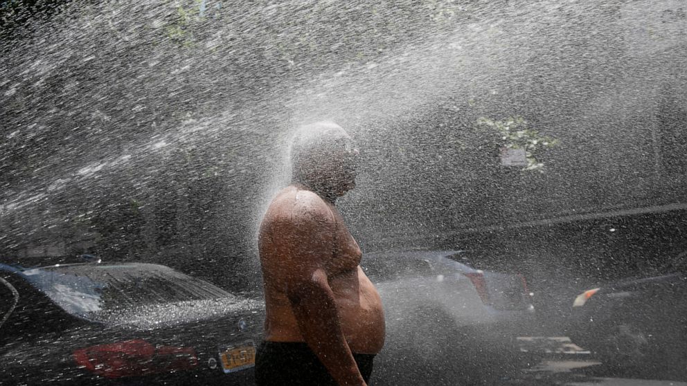 FILE - In this Tuesday, July 28, 2020 file photo, Rey Gomez cools off in the spray from a fire hydrant in New York, as the city opened more than 300 fire hydrants with sprinkler caps to help residents cool off during a heat wave. According to a study