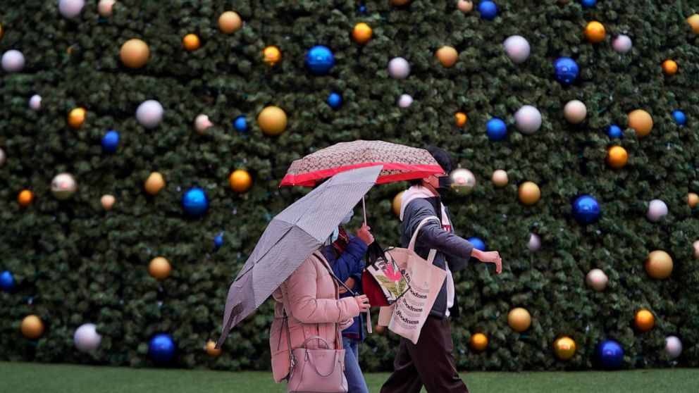 Pedestrians carry umbrellas as they walk past a large holiday tree outside of the Chase Center in San Francisco, Wednesday, Dec. 22, 2021. Rain and snow showers fell on Northern California on Wednesday in the first wave of a wet weather pattern that 