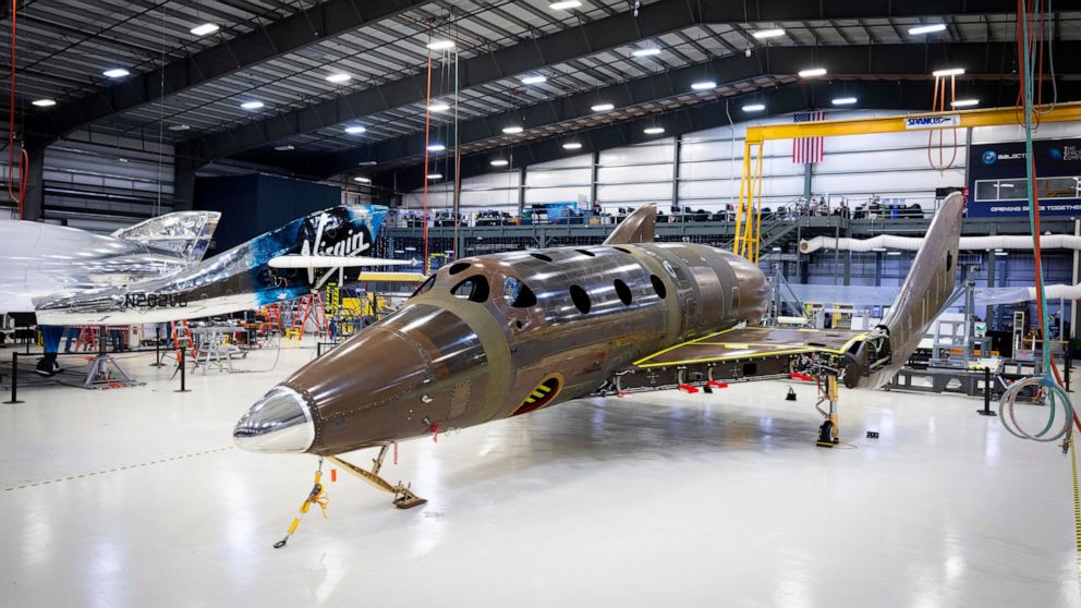 This photo released by Virgin Galactic Wednesday, Jan. 8, 2020, shows Virgin Galactic's next passenger spaceship standing on its landing gear in what is known as a weight-on-wheels test, in a hangar at the company's Mojave Air & Space Port in Mojave,