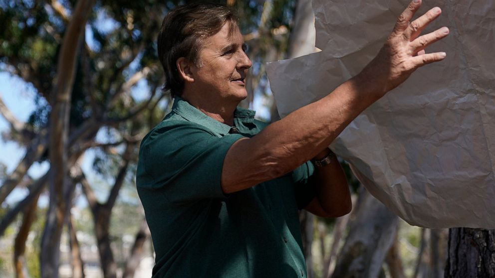 Dan Hirning, founding president of Firezat Inc., reaches for some of the material that protects homes, his company uses as a gust of wind passes, Thursday, Sept. 16, 2021, in Del Mar, Calif. Aluminum wraps designed to protect homes from flames are ge
