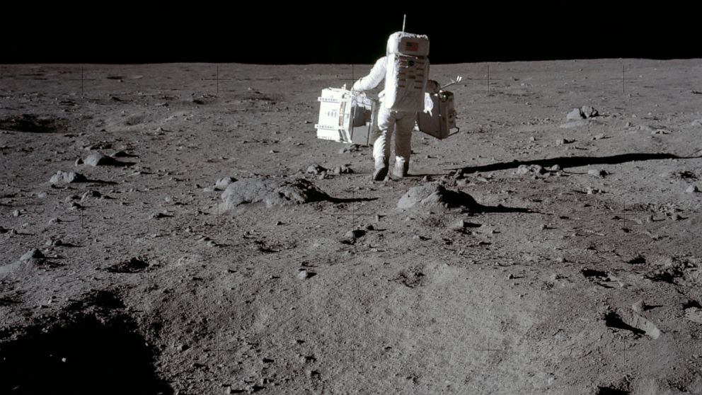 In this July 20, 1969 photo made available by NASA, lunar module pilot Buzz Aldrin carries a seismic experiments package in his left hand and the Laser Ranging Retroreflector to the deployment area on the surface of the moon at Tranquility Base. On T