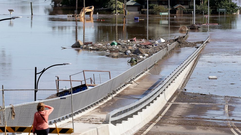 FILE - In this March 25, 2021, file photo, a woman looks at debris caught on a submerged bridge in Windsor, northwest of Sydney, Australia. Over recent times, Australia has endured droughts, fires, floods, even a plague of marauding mice.(AP Photo/Ri