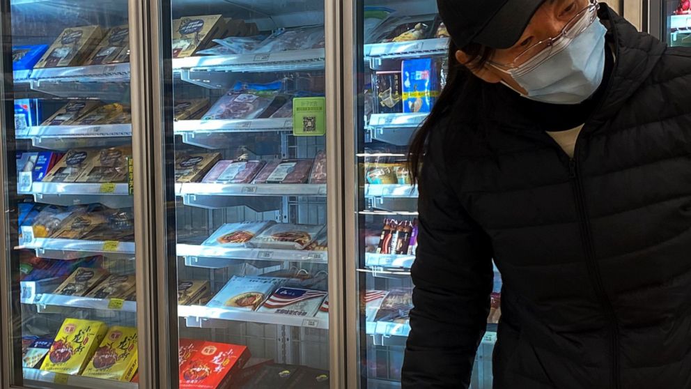 A woman wearing a face mask to help curb the spread of the coronavirus walks by a fridge displaying frozen meats at a supermarket in Beijing, Tuesday, Nov. 24, 2020. China has stirred controversy with claims it has detected the coronavirus on package