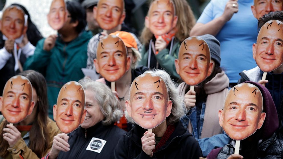 FILE - In this Oct. 31, 2018, file photo, demonstrators hold images of Amazon CEO Jeff Bezos near their faces during a Halloween-themed protest at Amazon headquarters over the company's facial recognition system, "Rekognition," in Seattle. San Franci