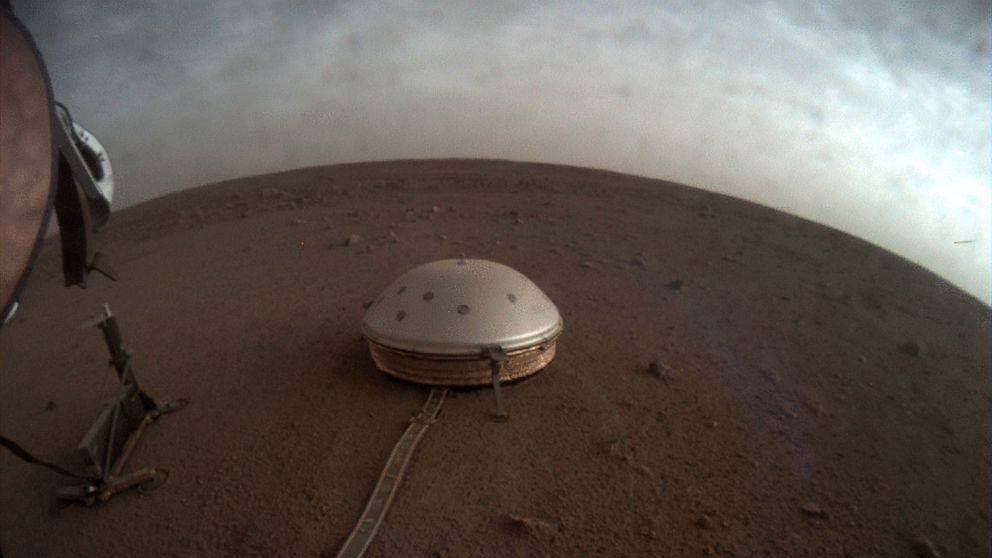 In this undated photo made available by NASA on Thursday, July 22, 2021, clouds drift over the dome-covered SEIS seismometer of the InSight lander on the surface of Mars. The quake-measuring device is providing the first detailed look at the red plan
