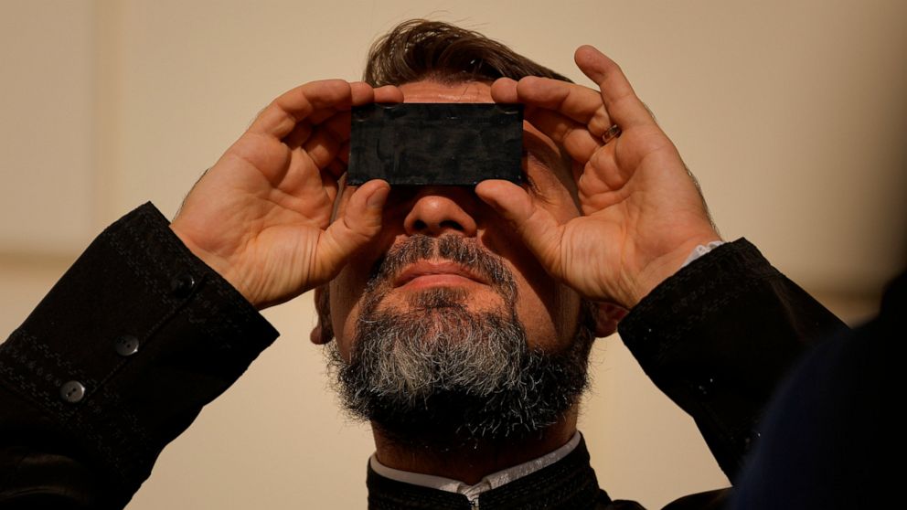 A priest looks through a welding filter during a partial solar eclipse in Bucharest, Romania, Tuesday, Oct. 25, 2022. People around the world gathered Tuesday to witness the last solar eclipse of the year, a phenomenon where the moon briefly casts a 