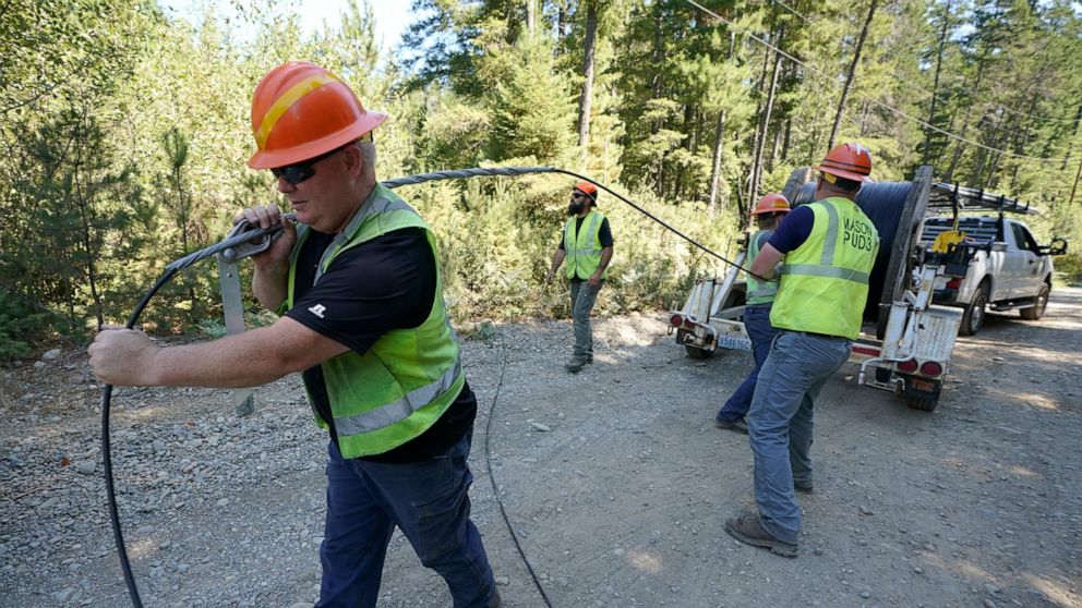 FILE - Carl Roath, left, a worker with the Mason County (Wash.) Public Utility District, pulls fiber optic cable off of a spool, as he works with a team to install broadband internet service to homes in a rural area surrounding Lake Christine near Be