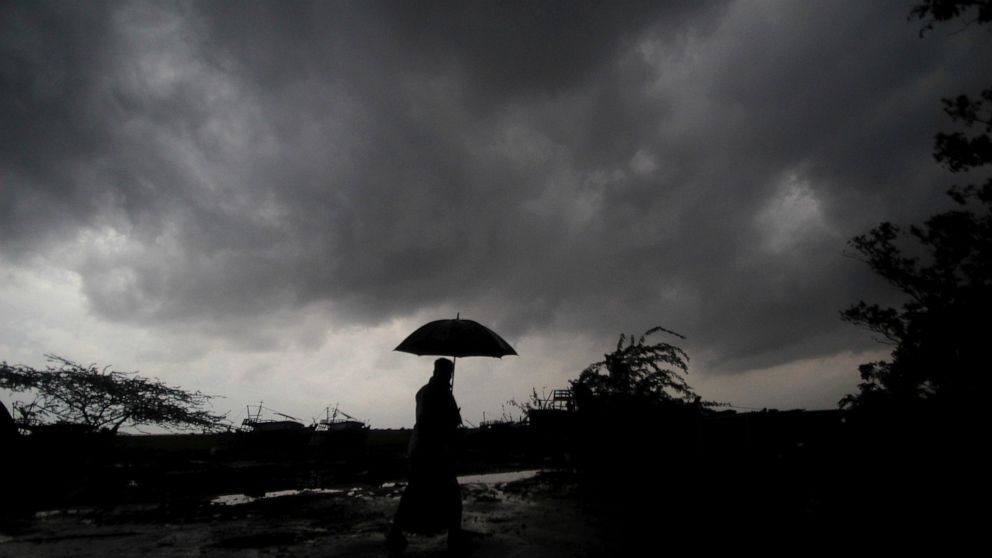 FILE - A villager holds an umbrella as dark clouds loom over Balasore district in Odisha, India, Tuesday, May 25, 2021, ahead of a powerful storm barreling toward the eastern coast. When it comes to measuring global warming, it’s not just the heat, i