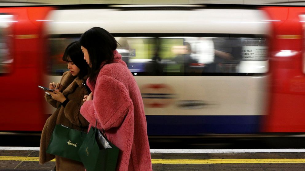 FILE - In this file photo dated Tuesday, Dec. 24, 2019, women use a cell phone on an underground platform in central London. Facebook's purchase of Giphy will hurt competition for animated images, U.K. regulators said Thursday Aug. 12, 2021, followin