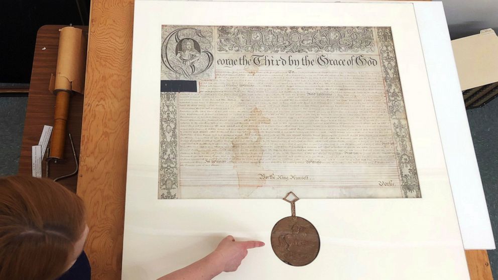 FILE - Rhode Island state archivist Ashley Selima points to the seal of King George III on a September 1772 proclamation in Providence, R.I., May 24, 2018. The document established a commission to investigate the burning of the British schooner HMS G