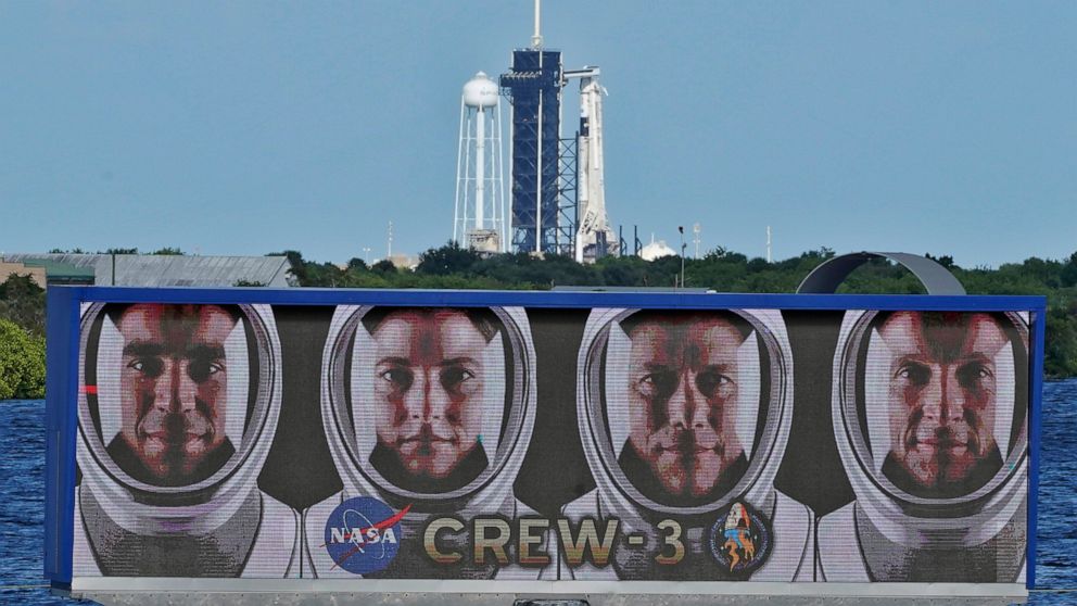 FILE - The official portraits of astronauts, from left, Raja Chari, Kayla Barron, Matthias Maurer, of Germany, and Tom Marshburn, are displayed as a SpaceX Falcon 9 rocket with the crew dragon capsule attached sits on Launch Pad 39-A at the Kennedy S