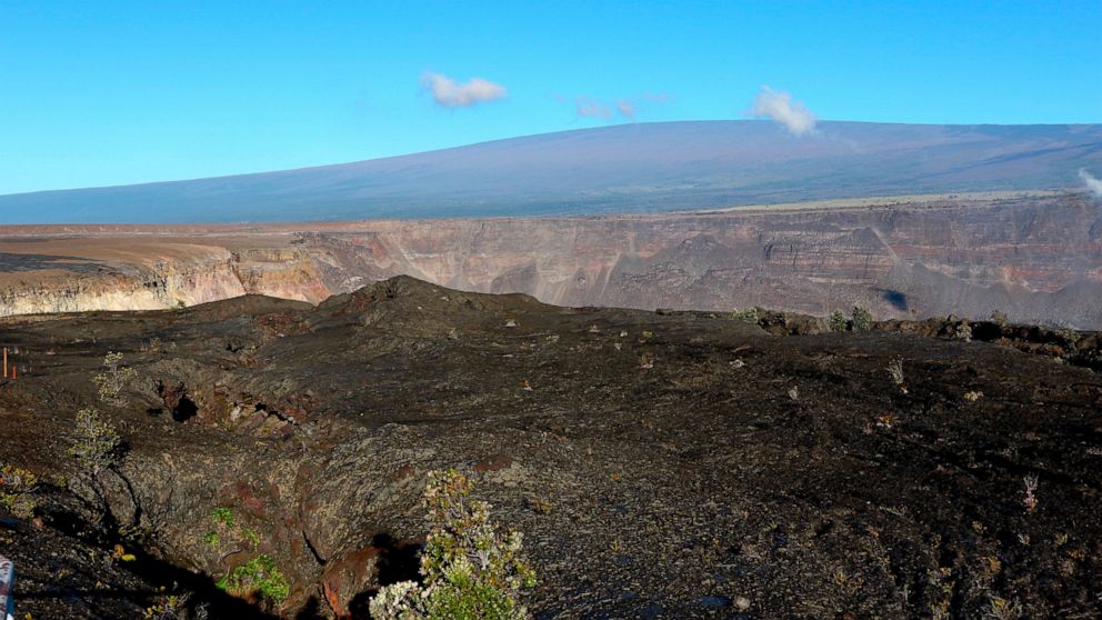 In this April 25, 2019 photo, Hawaii's Mauna Loa volcano, background, towers over the summit crater of Kilauea volcano in Hawaii Volcanoes National Park on the Big Island. Federal officials raised the alert level for Mauna Loa, the world's largest ac