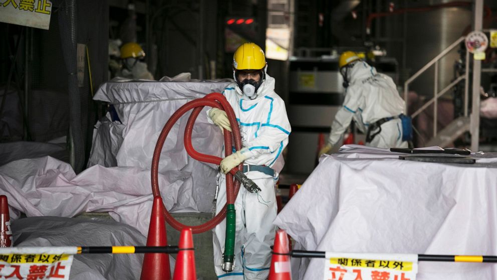 FILE - In this Feb. 12, 2020, file photo, a worker in a hazmat suit carries a hose while working at a water treatment facility at the Fukushima Dai-ichi nuclear power plant in Okuma, Fukushima Prefecture, Japan. Japanese Prime Minister Yoshihide Suga