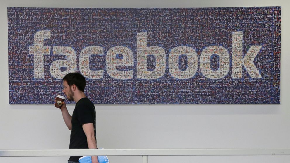A Facebook employee walks past a sign at Facebook headquarters in Menlo Park, Calif., March 15, 2013.