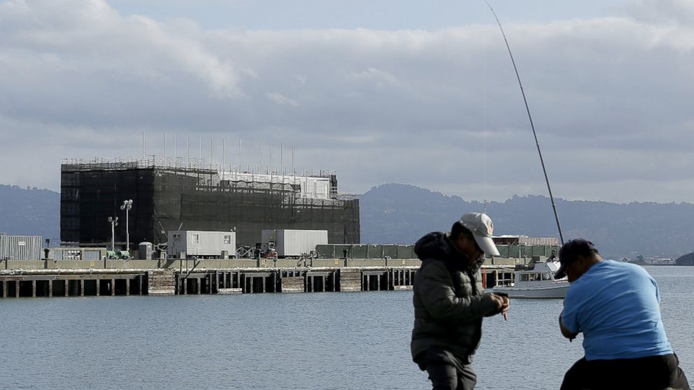 PHOTO: Two men fish in the water in front of a barge on Treasure Island in San Francisco, Oct. 29, 2013.