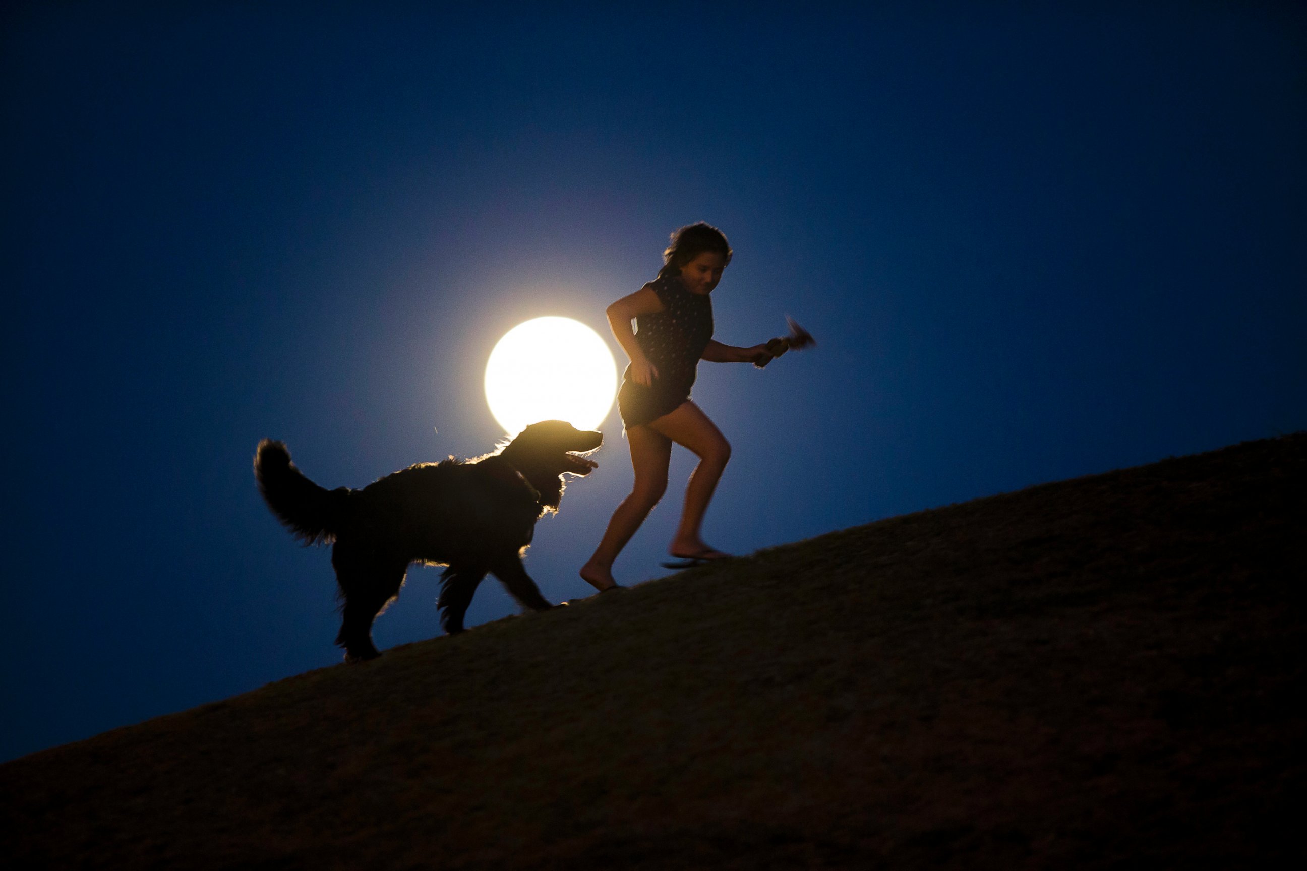 PHOTO: A girl plays with a dog as a perigee moon, also known as a supermoon, rises in Madrid, Aug. 10, 2014.