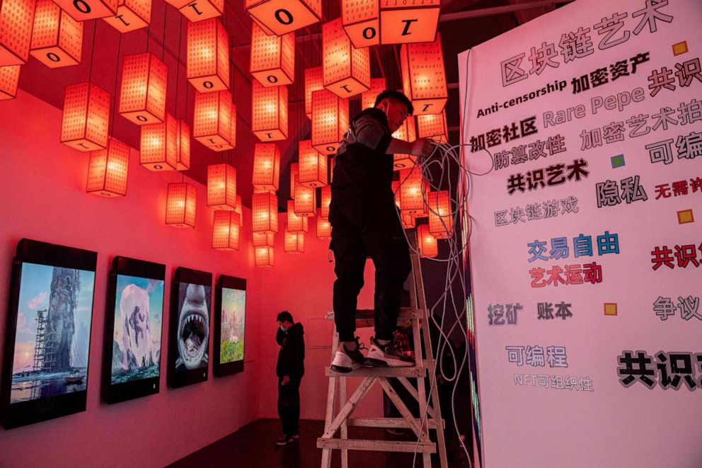 PHOTO: Staff make preparations next to digital paintings by U.S. artist Beeple at a crypto art exhibition entitled "Virtual Niche: Have You Ever Seen Memes in the Mirror?" ahead of its opening in Beijing on March 26, 2021.