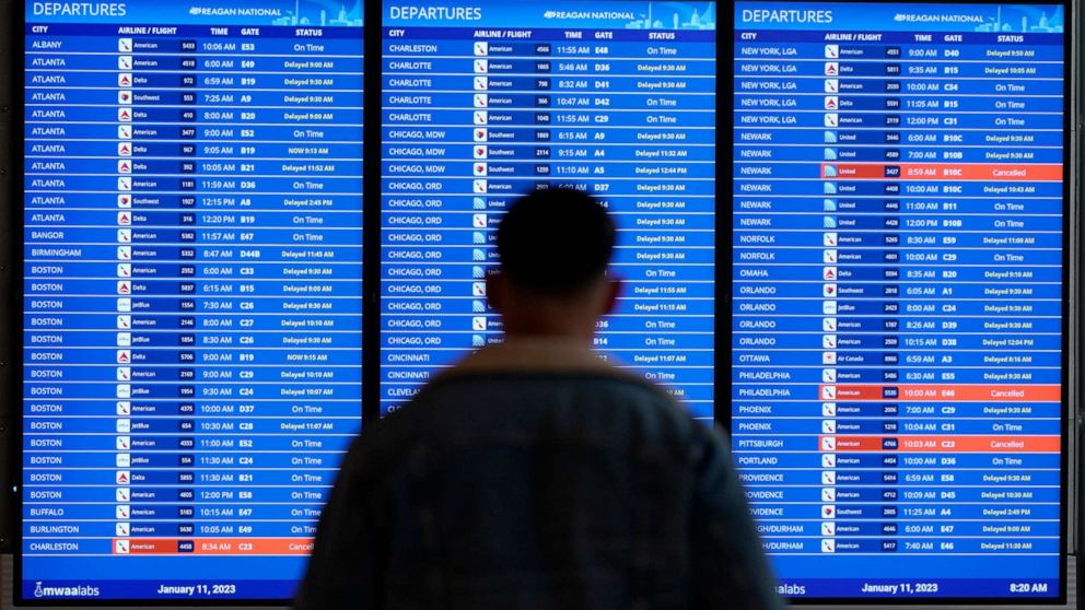 FOTO: Seorang pelancong melihat papan penerbangan dengan penundaan dan pembatalan di Bandara Nasional Ronald Reagan Washington di Arlington, Va., 11 Januari 2023.