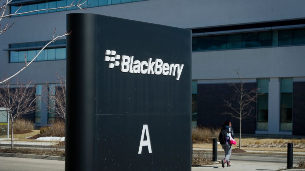 An employee crosses the street near signage displayed at BlackBerry Ltd. headquarters in Waterloo, Canada, March 19, 2015.