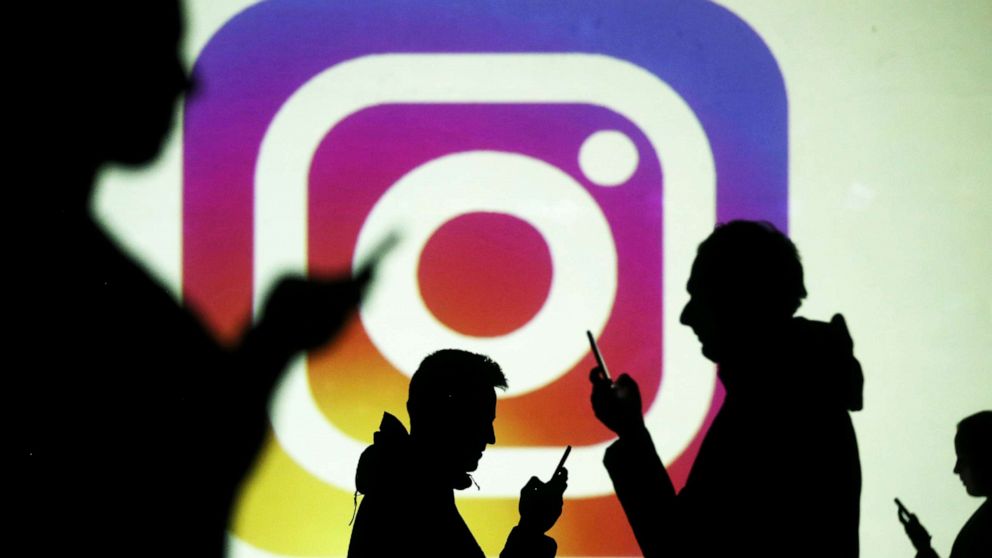 PHOTO: Silhouettes of mobile users are seen next to a screen projection of Instagram logo in this picture illustration taken March 28, 2018.