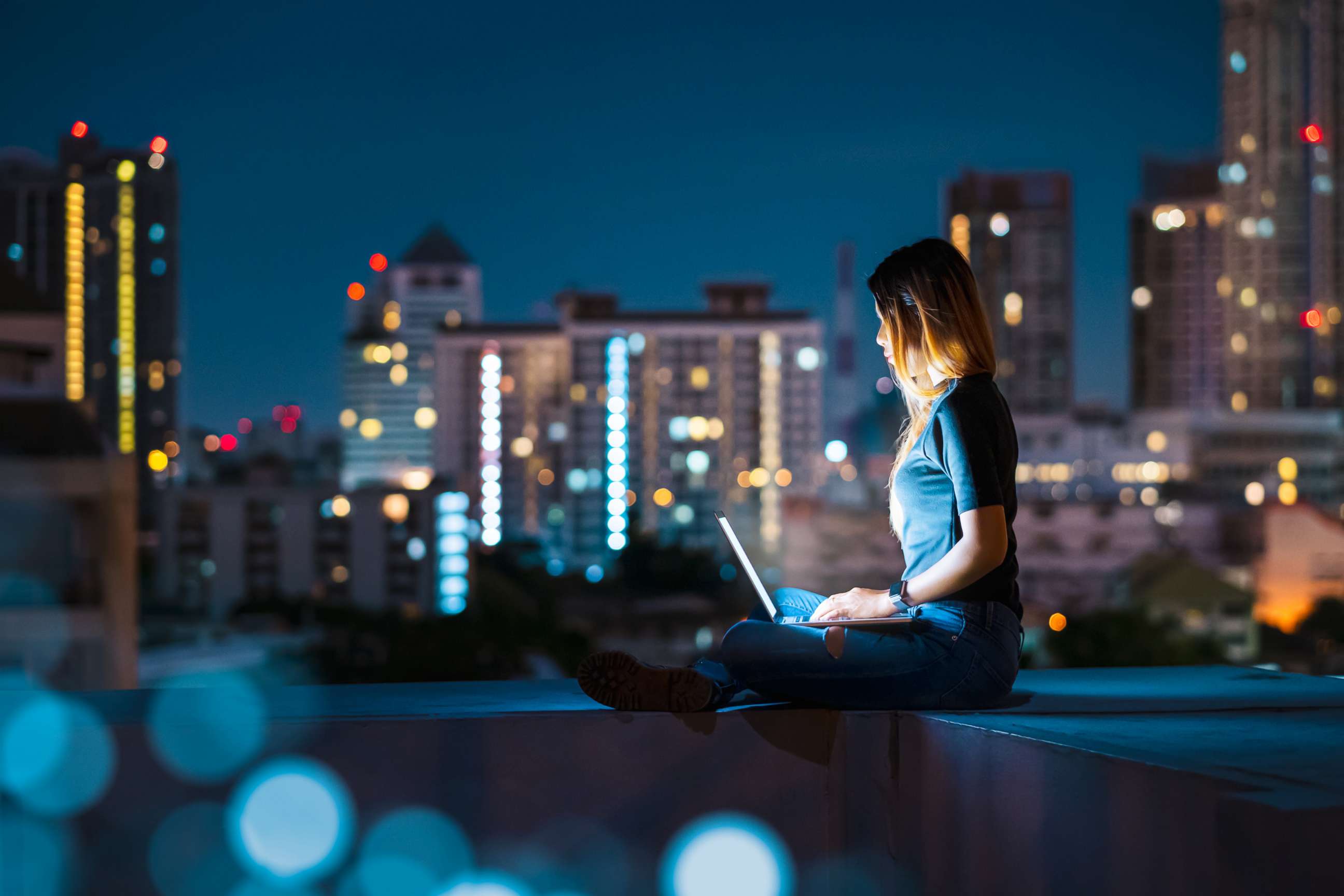 PHOTO: A stock photo of a woman using a laptop on the rooftop of building.