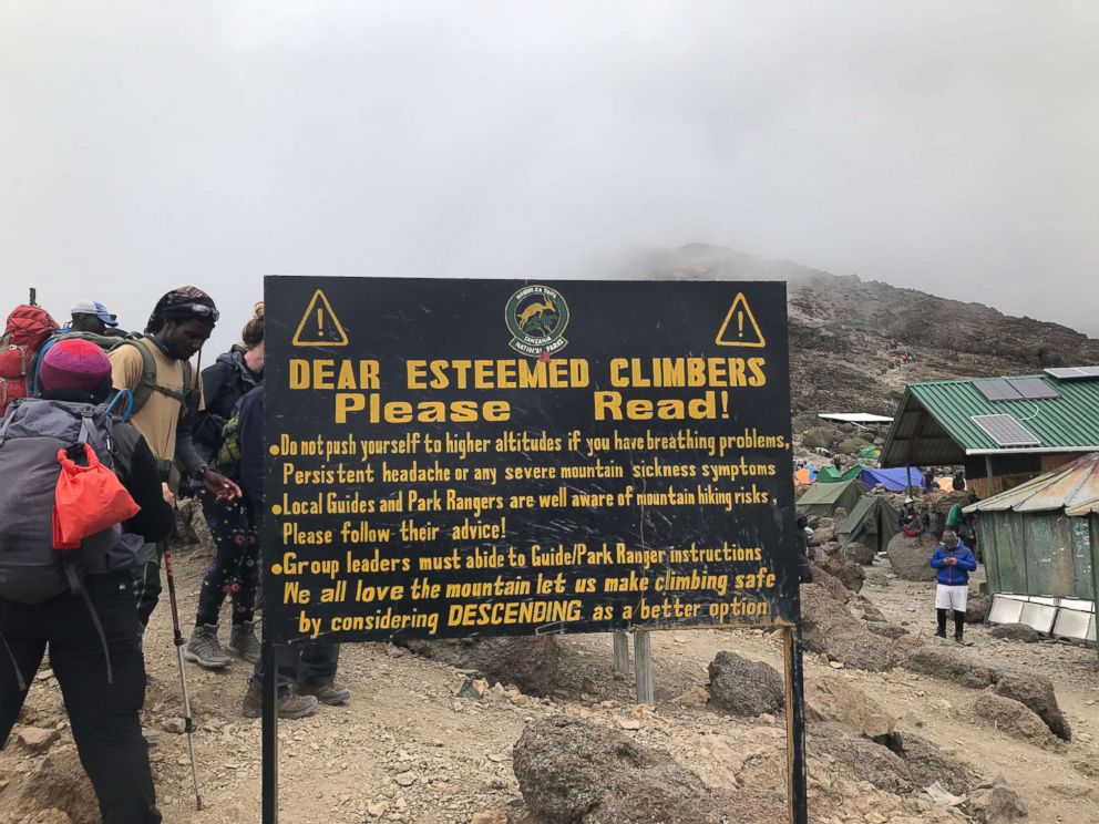 PHOTO: People walk near a warning sign at Barafu Camp on Mount Kilimanjaro, Tanzania, typically the final camp used before a summit push, in February 2019.