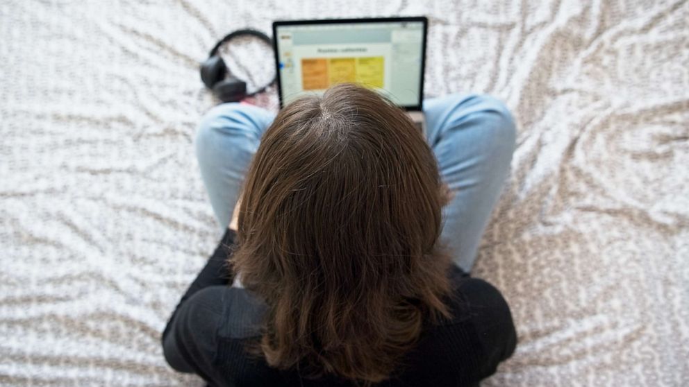 FOTO: Een tienermeisje typt op haar laptop terwijl ze op haar bed zit