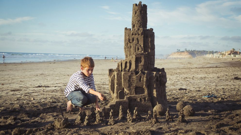 A boy puts builds a sandcastle on the beach in San Diego.