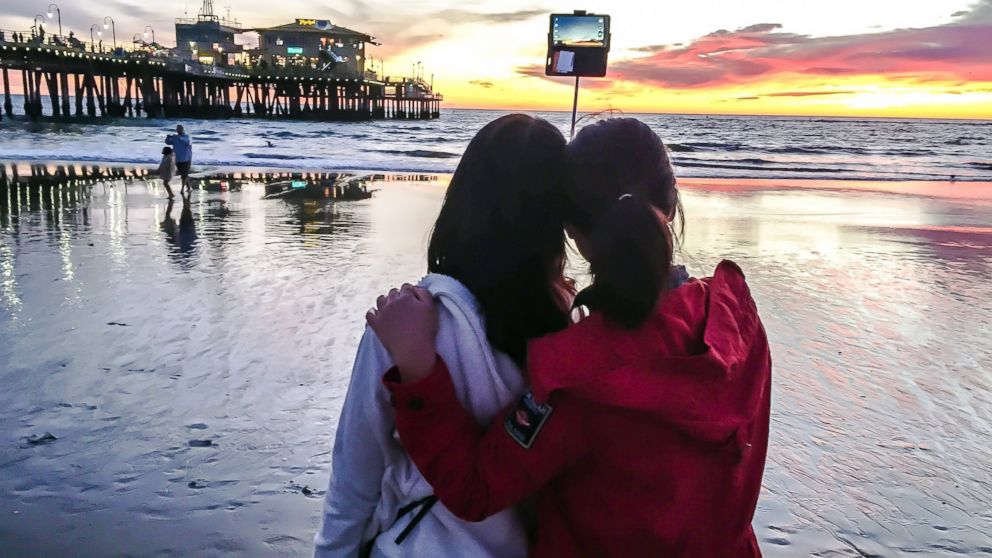 Two tourists take a photo with a selfie stick on the beach in Santa Monica, Calif., Jan. 22, 2015. sunset.