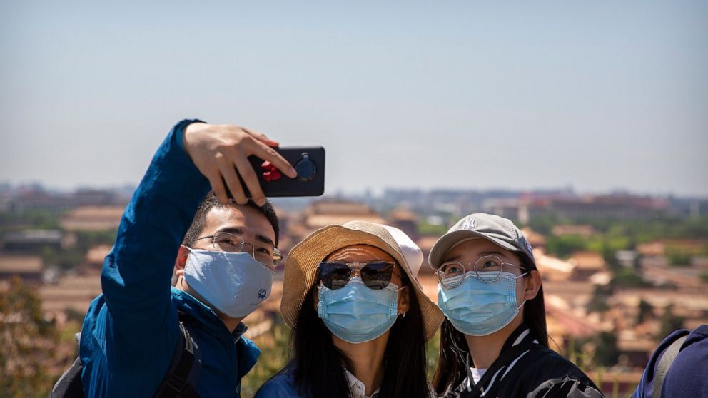 Visitors wearing face masks pose for a selfie at a viewing area overlooking the Forbidden City at a public park in Beijing, Saturday, May 1, 2021. Chinese tourists are expected to make a total of 18.3 million railway passenger trips on the first day 