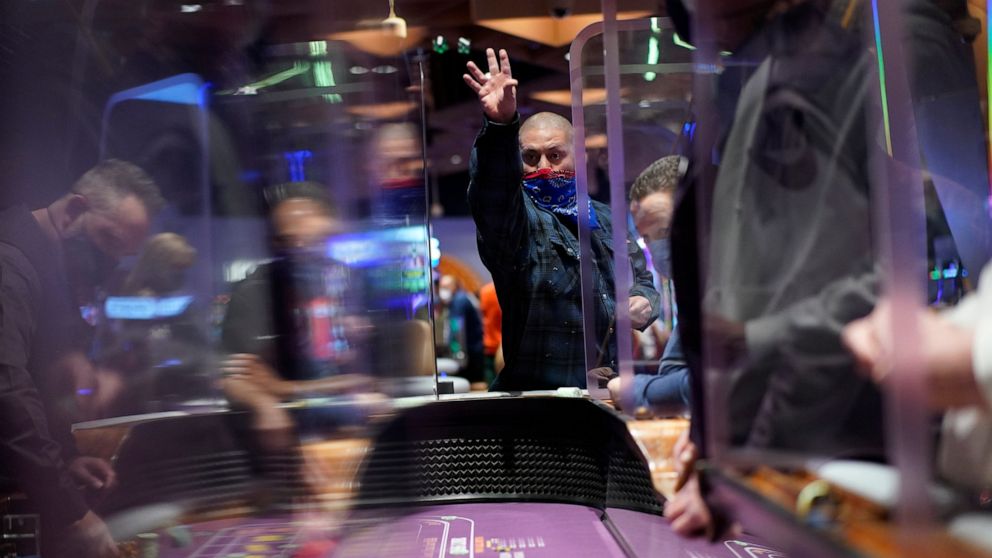 FILE - In this March 25, 2021, file photo, people play craps while wearing masks and between Plexiglas partitions as a precaution against the coronavirus at the opening night of the Virgin Hotels Las Vegas in Las Vegas. Las Vegas is bouncing back to 