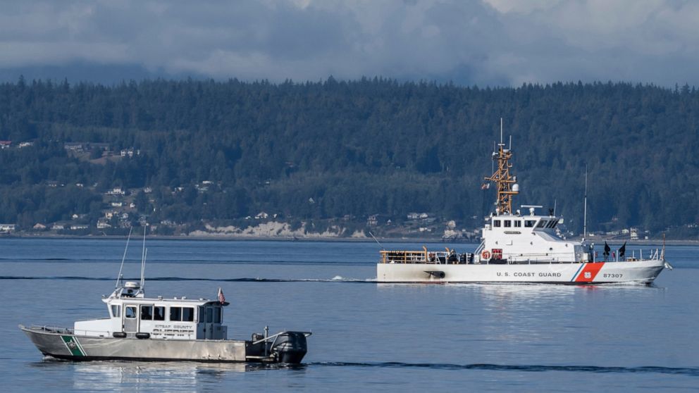 A U.S. Coast Guard boat and Kitsap, Wash., County Sherrif boat search the area, Monday, Sept. 5, 2022, near Freeland, Wash., on Whidbey Island north of Seattle where a chartered floatplane crashed the day before. The plane was carrying 10 people and 